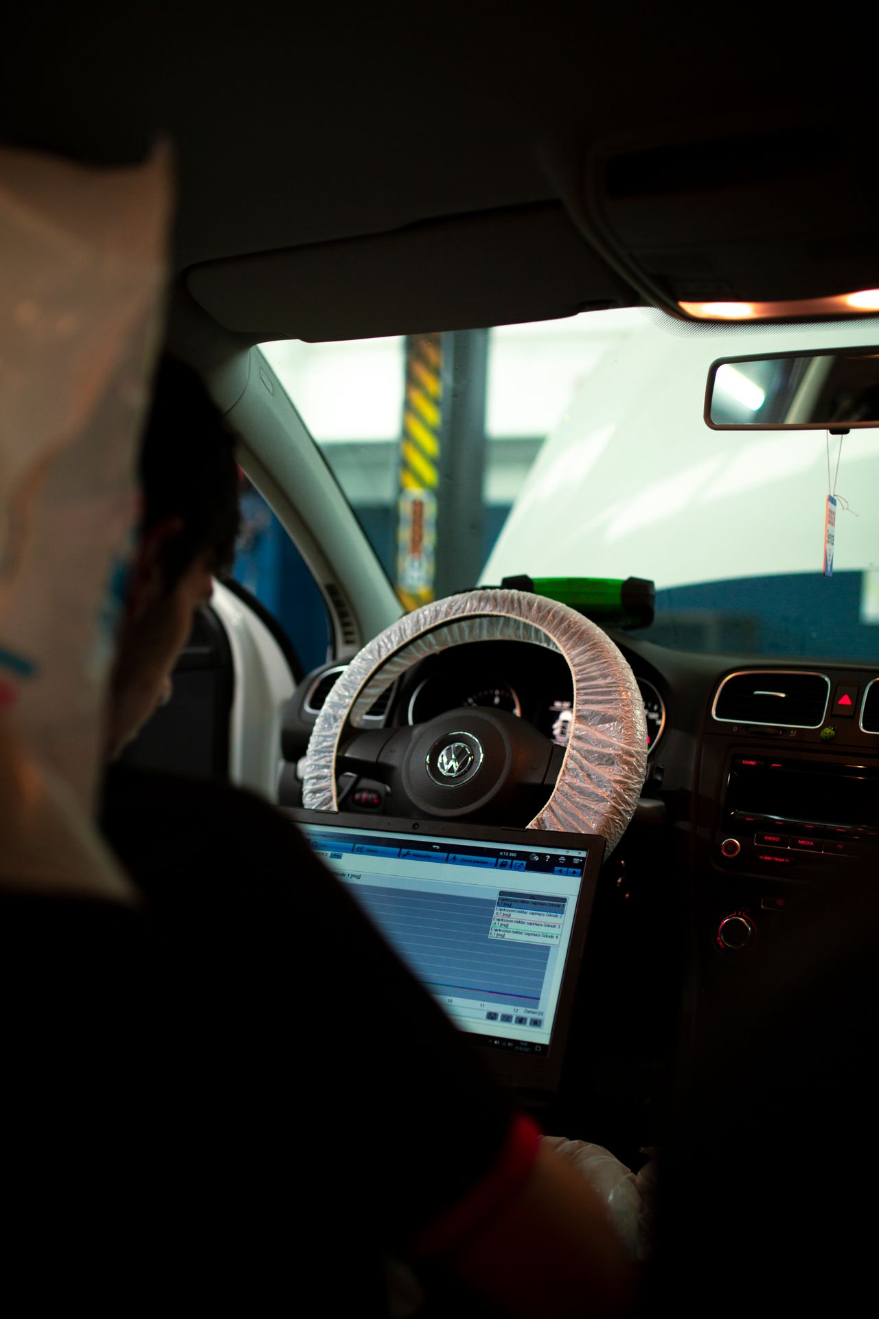 Automotive technician using a laptop inside a vehicle for digital diagnostics in a real workshop