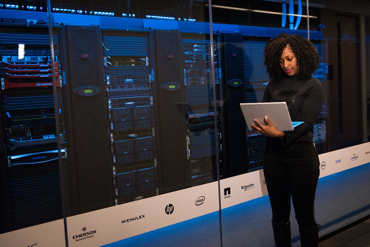 Software engineer using a laptop beside server racks in a real data-centre environment
