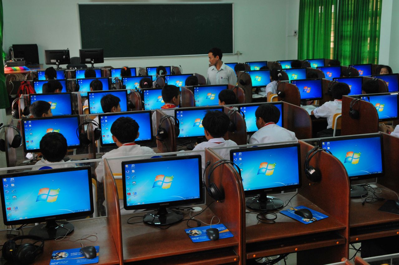 Students learning in a real computer lab with a teacher instructing digital technology
