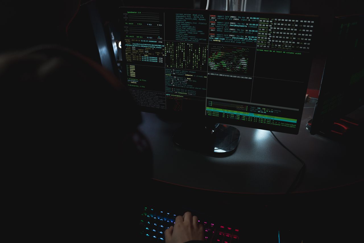 Cybersecurity professional reviewing code across multiple monitors in a real technology workspace